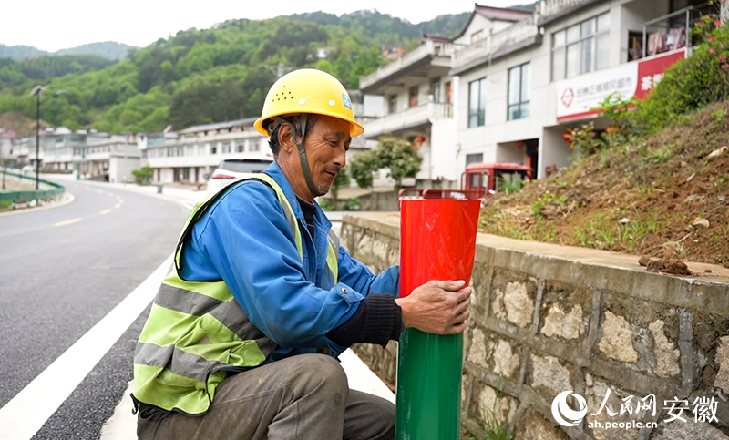 大灣村村民陶元佳正在路邊為護欄張貼反光貼。人民網記者 王銳攝